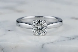 Bague de fiançailles en or blanc avec diamant solitaire posée sur marbre blanc, illustrant l'éclat caractéristique de l'or blanc rhodié