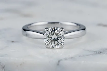 Bague de fiançailles en or blanc avec diamant solitaire posée sur marbre blanc, illustrant l'éclat caractéristique de l'or blanc rhodié